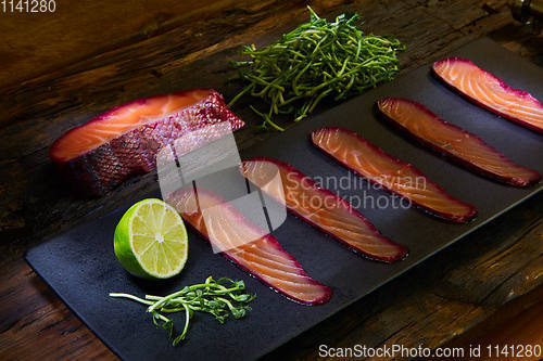 Image of Sliced salmon fillet, salted with beetroot juice, served on whole wheat with salad leaves, sea salt and pepper over metal surface. Top view