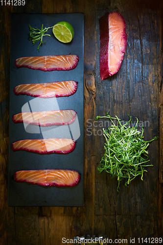 Image of Sliced salmon fillet, salted with beetroot juice, served on whole wheat with salad leaves, sea salt and pepper over metal surface. Top view