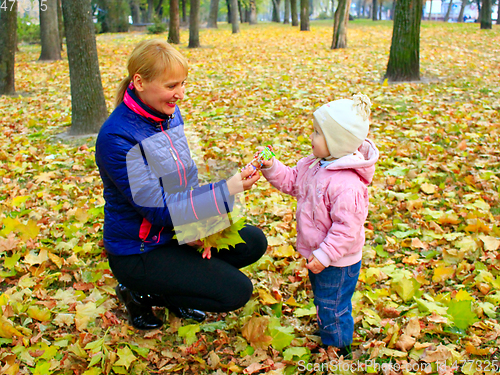 Image of woman gives her daughter a sweet in the autumn park