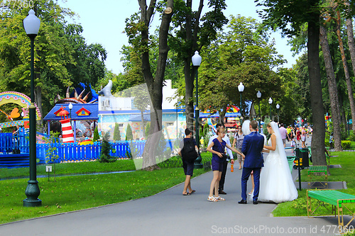 Image of married couple with friends walk in park with big trees