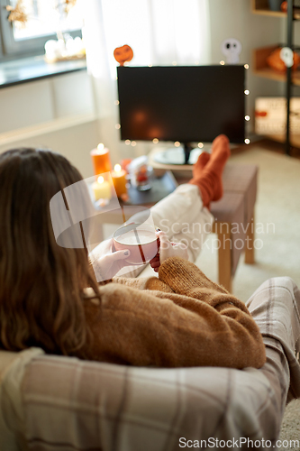 Image of woman watches tv and drinks cocoa on halloween