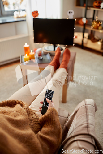 Image of young woman watching tv at home on halloween