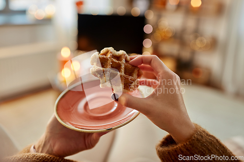 Image of hands of young woman eating waffle at home
