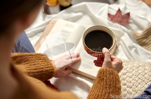 Image of woman drinking coffee and reading book in autumn