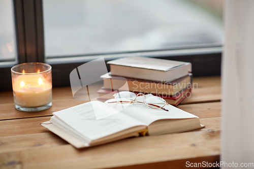 Image of books, glasses and candle burning on window sill