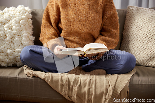 Image of woman in warm sweater reading book at home