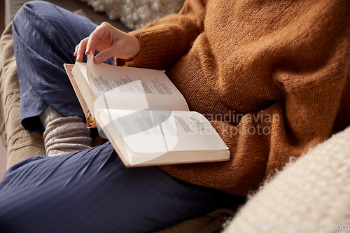 Image of woman in warm sweater reading book at home