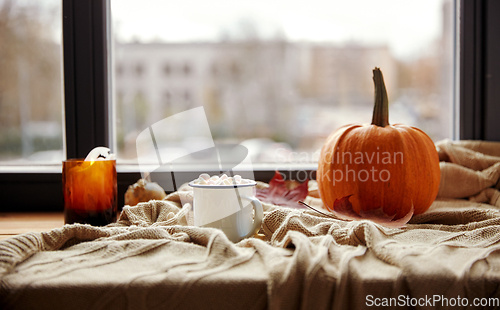 Image of cup of marshmallow, candle and pumpkin on window