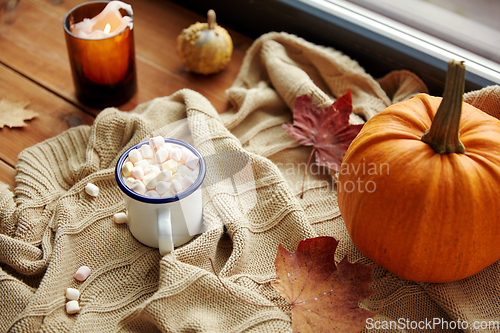 Image of cup of marshmallow, candle and pumpkin on window