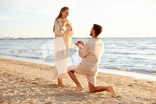 Image of man with ring making proposal to woman on beach