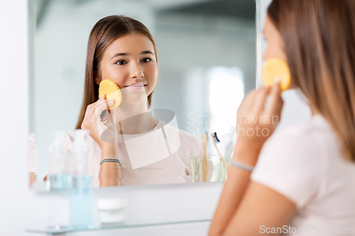 Image of teenage girl cleaning face with sponge at bathroom