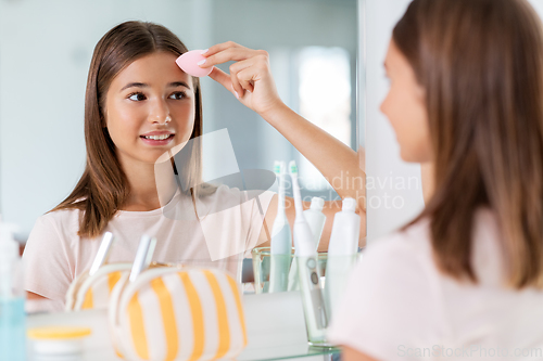 Image of teenage girl applying foundation to face