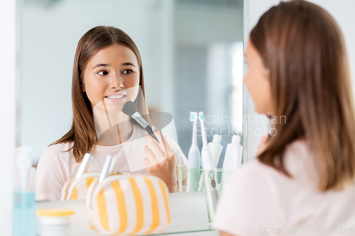 Image of teenage girl applying powder to face at bathroom