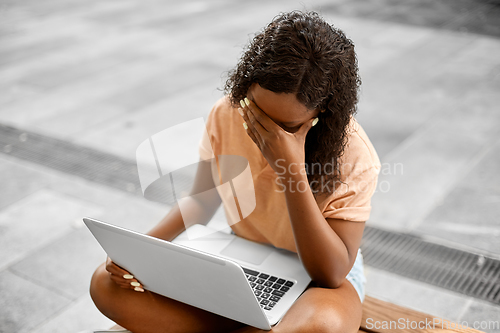Image of stressed african student girl with laptop in city
