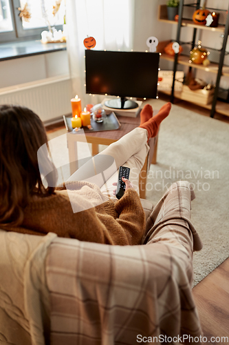 Image of young woman watching tv at home on halloween