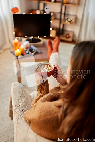 Image of woman watches tv and drinks cocoa on halloween