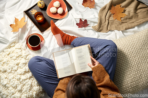 Image of young woman reading book at home in autumn