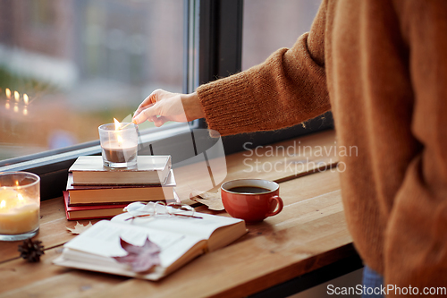 Image of hand with match lighting candle on window sill