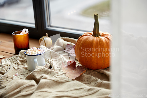 Image of cup of marshmallow, candle and pumpkin on window