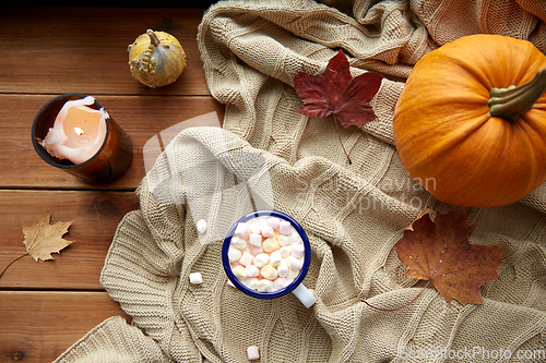 Image of cup of marshmallow, candle and pumpkin on window