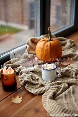 Image of cup of marshmallow, candle and pumpkin on window