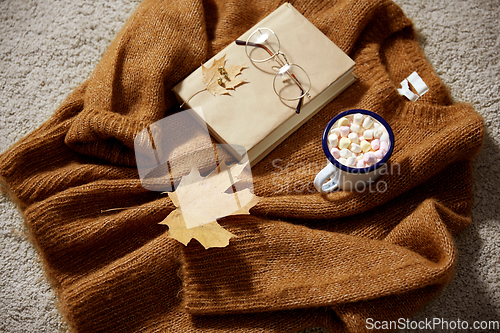 Image of cup of marshmallow, book and glasses on sweater