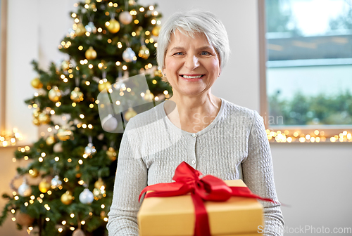 Image of smiling senior woman with christmas gift at home