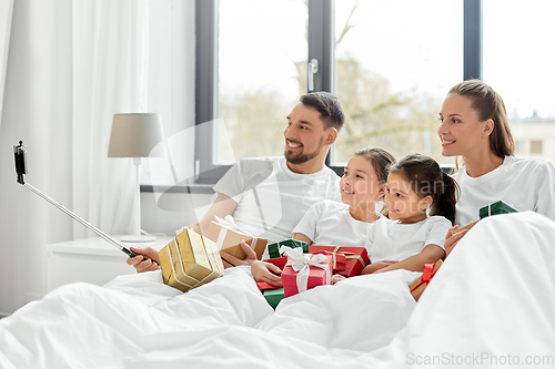 Image of family with christmas gifts taking selfie in bed