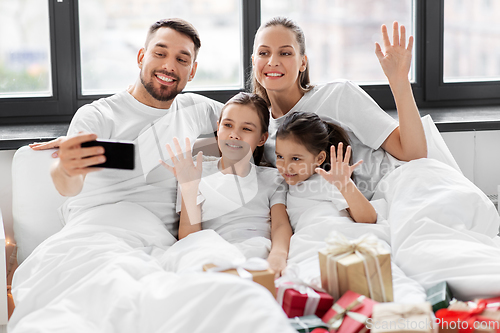 Image of family with christmas gifts taking selfie in bed