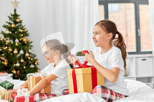 Image of happy sisters with christmas gifts in bed at home