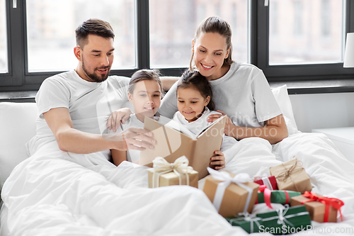 Image of happy family reading book in bed on christmas