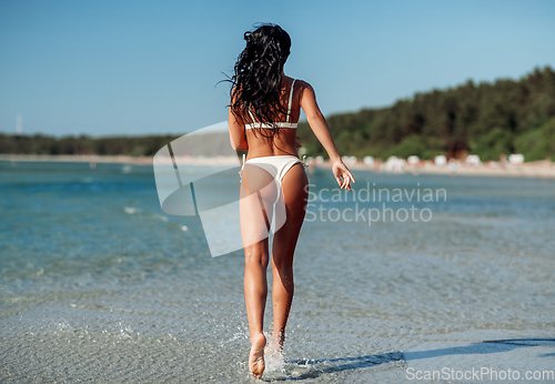 Image of young woman in bikini swimsuit running on beach