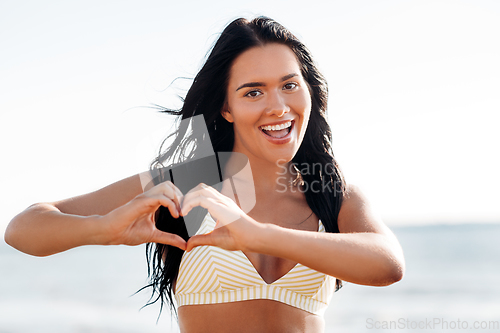 Image of smiling young woman in showing hand heart on beach