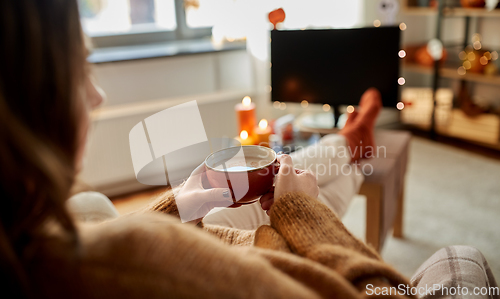 Image of woman watches tv and drinks cocoa on halloween