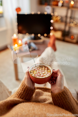 Image of woman watches tv and drinks cocoa on halloween