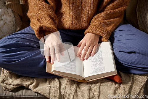 Image of woman in warm sweater reading book at home