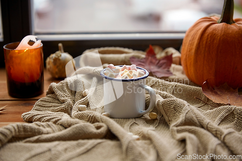 Image of cup of marshmallow, candle and pumpkin on window