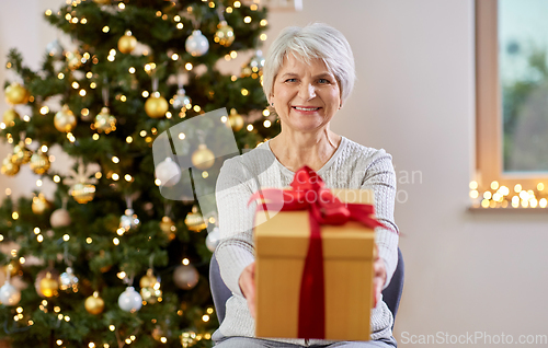 Image of happy senior woman with christmas gift at home