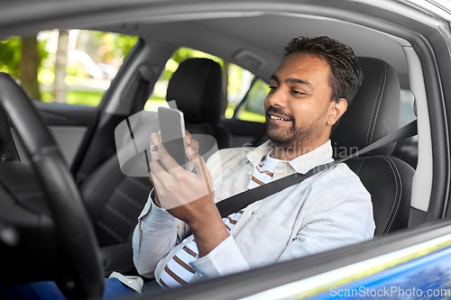 Image of smiling indian man in car using smartphone