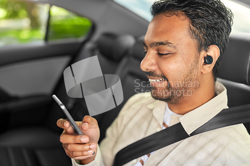 Image of passenger with earphones and cellphone in taxi car