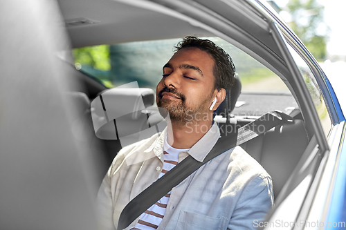 Image of indian male passenger with earphones in taxi car