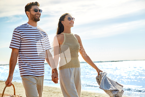 Image of happy couple with picnic basket walking on beach