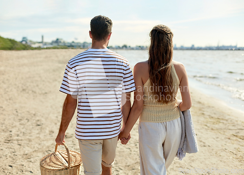 Image of happy couple with picnic basket walking on beach