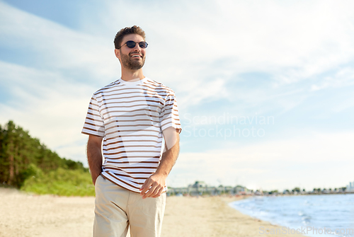 Image of young man in sunglasses walking along summer beach