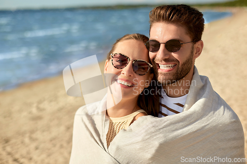 Image of happy couple covered with blanket hugging on beach