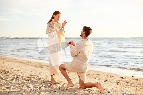 Image of man with ring making proposal to woman on beach