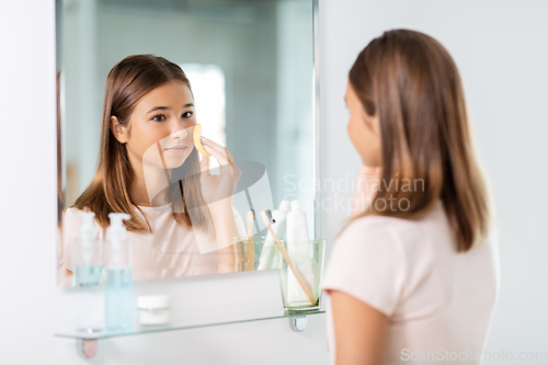 Image of teenage girl cleaning face with sponge at bathroom