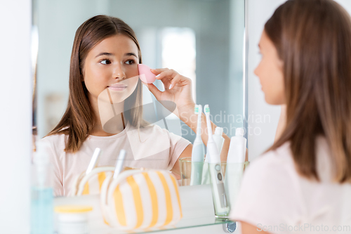 Image of teenage girl applying foundation to face