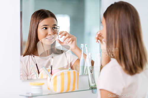 Image of teenage girl curling her lashes at bathroom