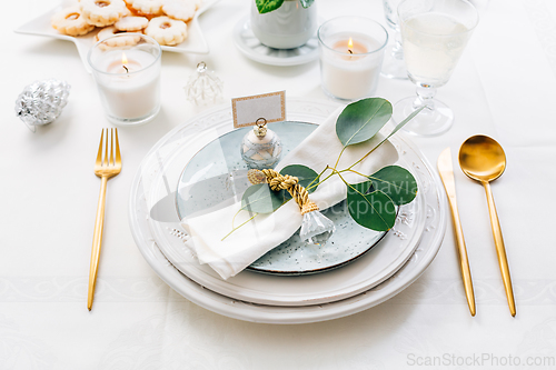 Image of Christmas table setting with eucalyptus, cutlery and candles in white and green tone